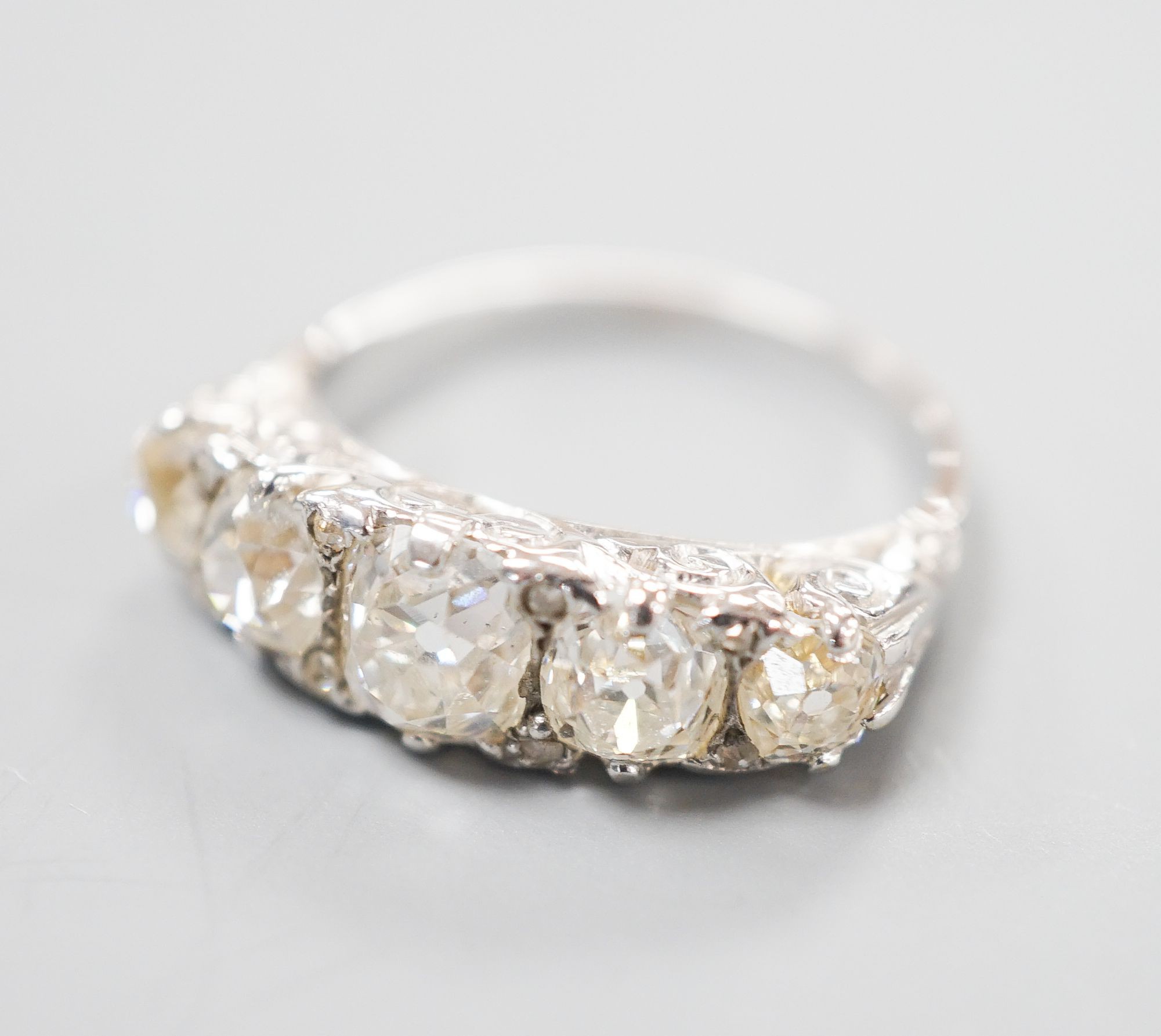 A white metal and graduated five stone old cut diamond set half hoop ring, with diamond chip spacers, size L, gross weight 3.7 grams.